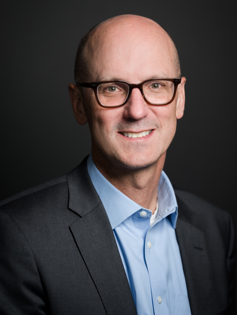 Photo of Joe Wright, Chief Commercial Officer, on a dark background in a blue button down shirt